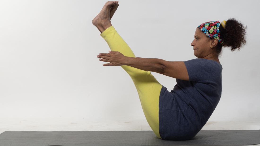 Tasneem in boat pose on a yoga mat